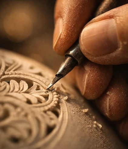 Close-up of a craftsman's hands hand-carving an ornate floral pattern into wood
