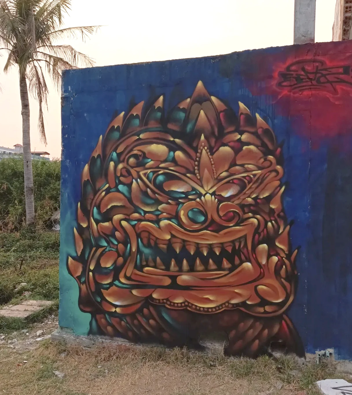 Ornate gold and teal demon mask mural painted on an outdoor wall in Cambodia